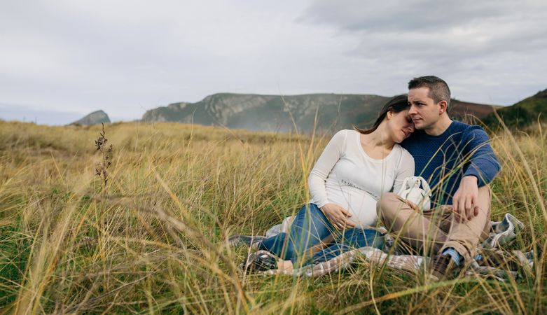 Pregnant woman with partner resting on the meadow