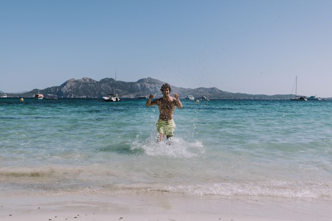 Man in swimsuit running in water on seashore