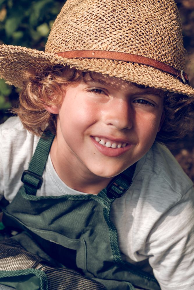 Cheerful preteen boy in wicker hat and apron