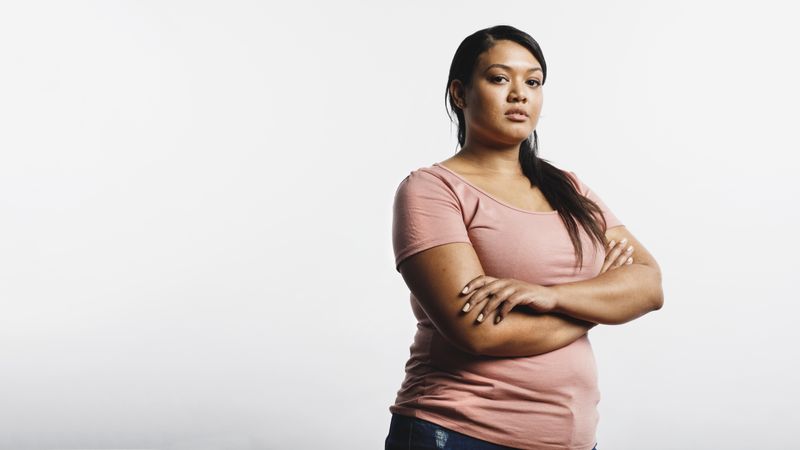 Woman in tshirt standing against neutral background with arms crossed