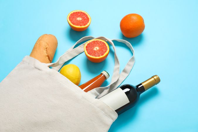 Eco bag with bottle of wine, juice, fruits and baguette on color background, space for text