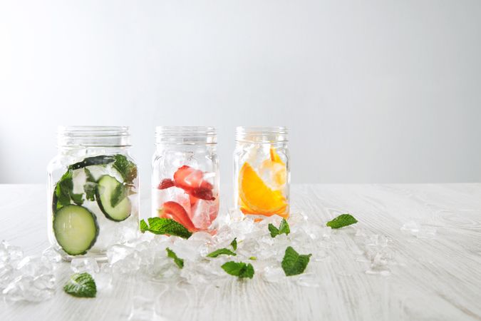 Three mason jars of infused water with distilled water bottle surrounded with copy space