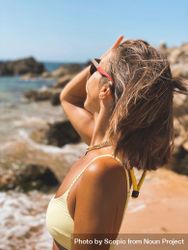 Side view of blonde woman in yellow bikini wearing sunglasses standing on beach 5Rz1W5