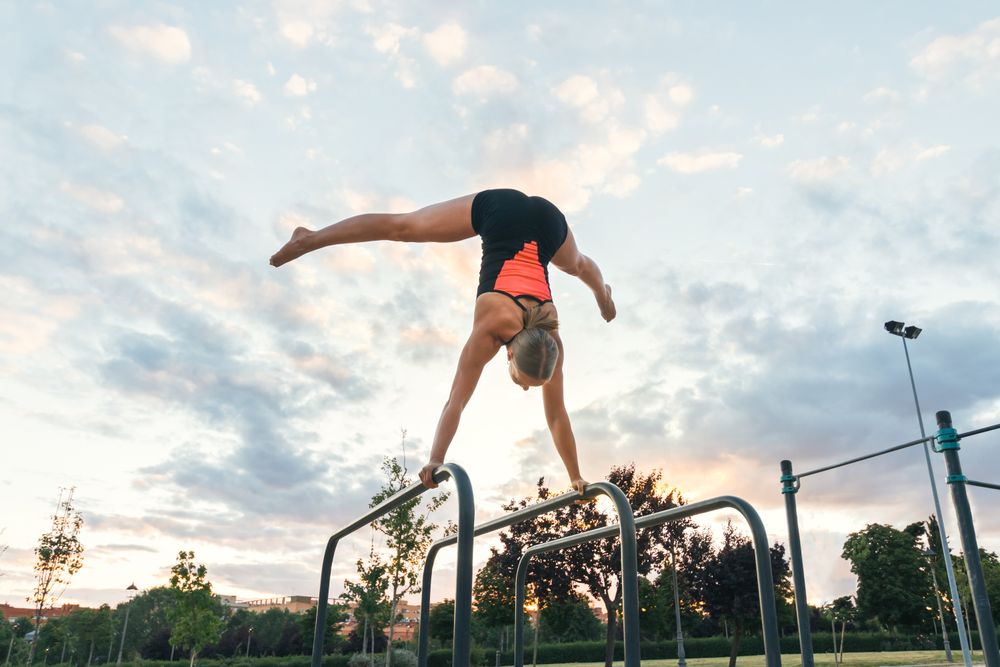 female athlete doing handstand on parallel bars