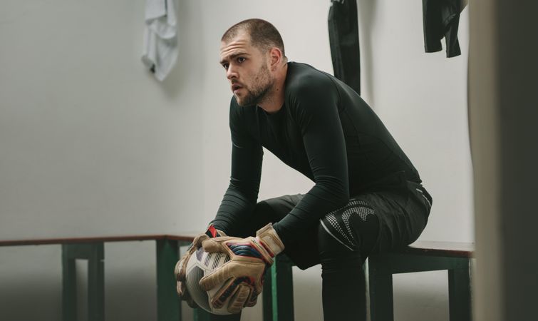 Goalkeeper sitting in a room holding a football and thinking