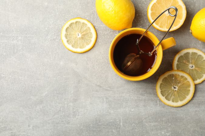 Cup of tea and lemons on grey background, space for text