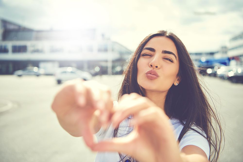 Brunette woman pushing lips making heart shape with hand