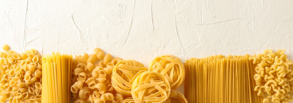 Different pasta on light background, space for text. Dry uncooked whole pasta