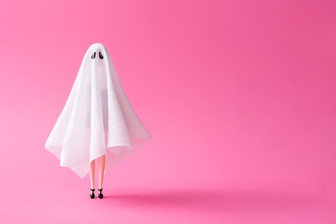 Doll under ghost sheet costume against pastel pink background