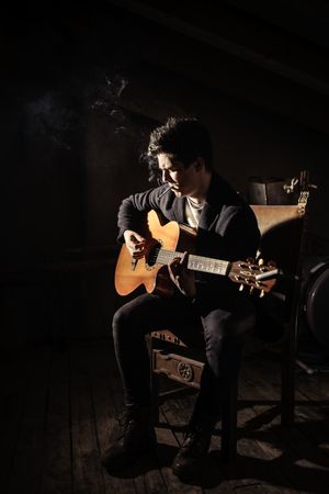 Man with guitar and cigarette sitting on chairs