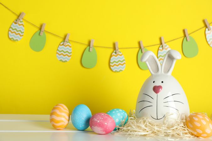 Decorated bunny and Easter eggs on table against color background
