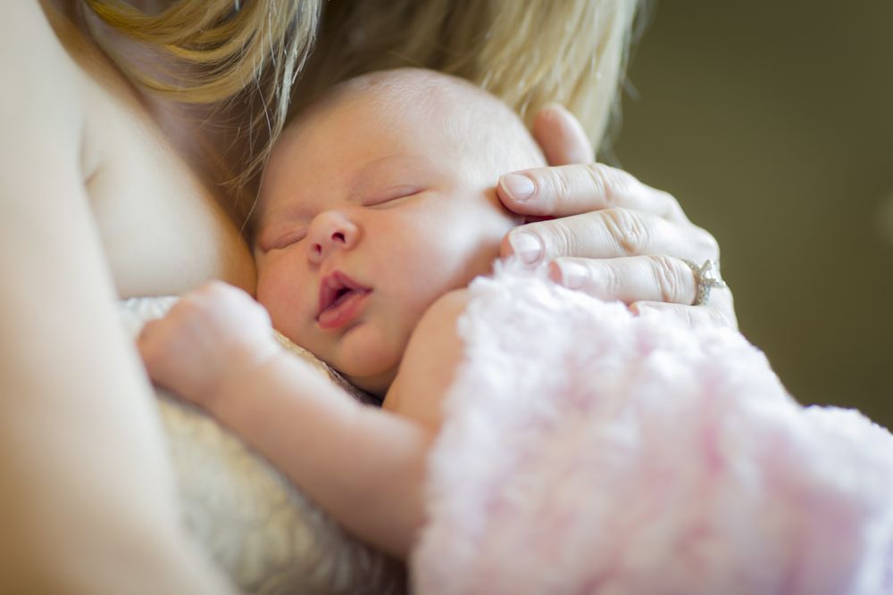 Hands of Mother Holding Her Newborn Baby Girl To Her Chest