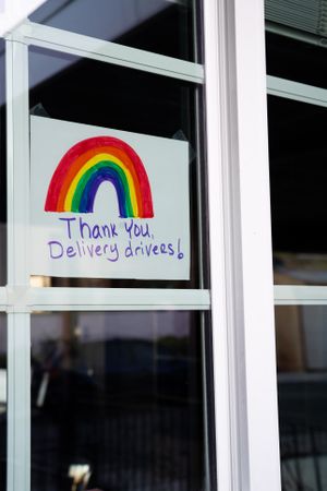 Horizontal shot of sign with rainbow and hand letters taped inside home window during lockdown