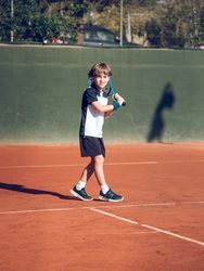 Preteen boy standing on hard court with racket playing tennis