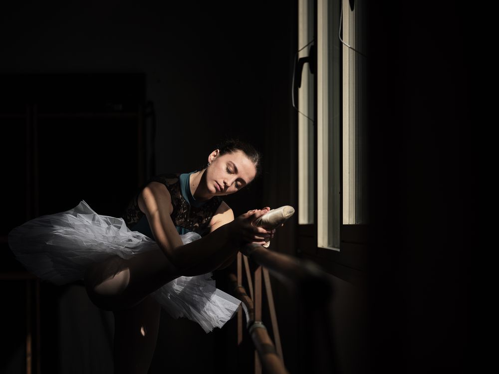 Young ballerina stretching leg on barre in dark room
