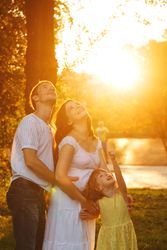 Young family looking up in park at magic hour with daughter pointing