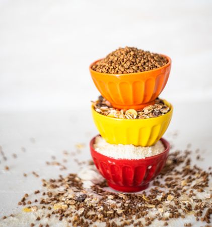 Side view of pile of three colorful ceramic bowls full of different grains