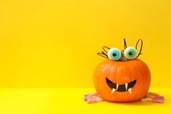 Decorated pumpkin with candy eyes on yellow background