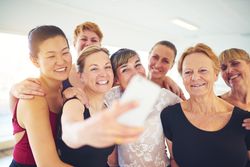 Group of smiling women pose for selfie in bright dance studio