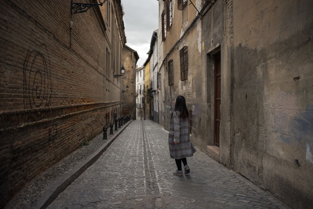 Woman walking on aged empty alleyway with old buildings