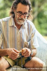 Mature man with beard knitting while sitting on chair 412lLb