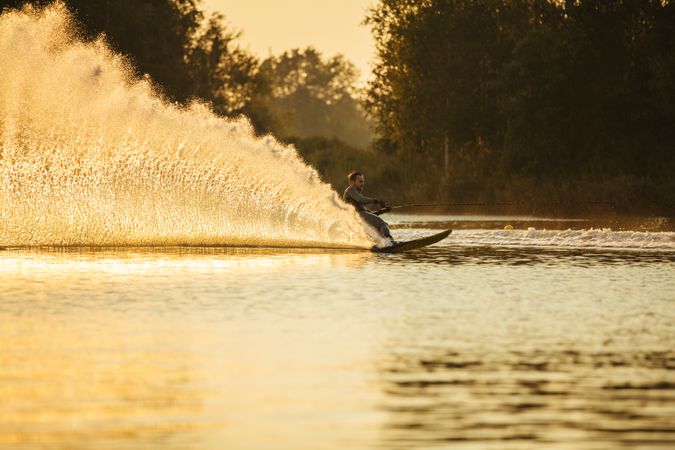 Man water skiing at sunset at a large lake with trees in the background