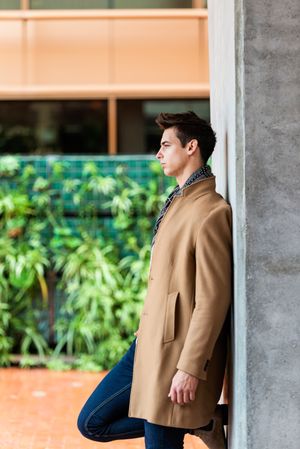 Side view of handsome man wearing camel coat and scarf looking away against cement wall