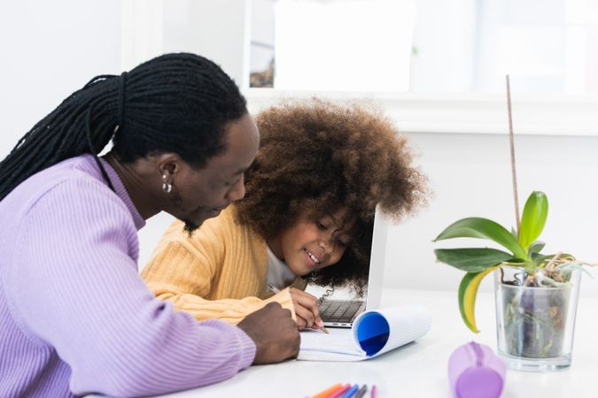 Black father helping daughter with homework on laptop