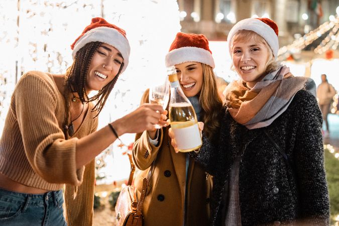 Three friends celebrating with champagne at a Christmas market, one looking at the camera.