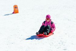 Child in pink snow suit going down a snowy hill in a red sled