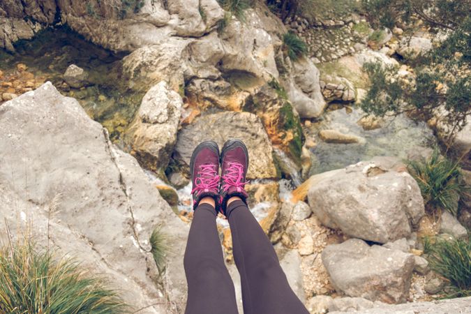 Crop female traveler sitting on rocky cliff with growing grass