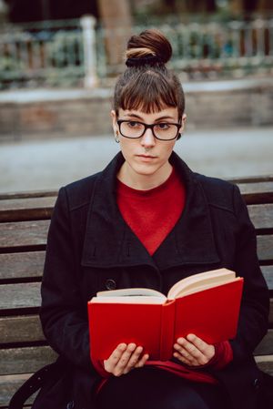 Young woman reading book on bench in park