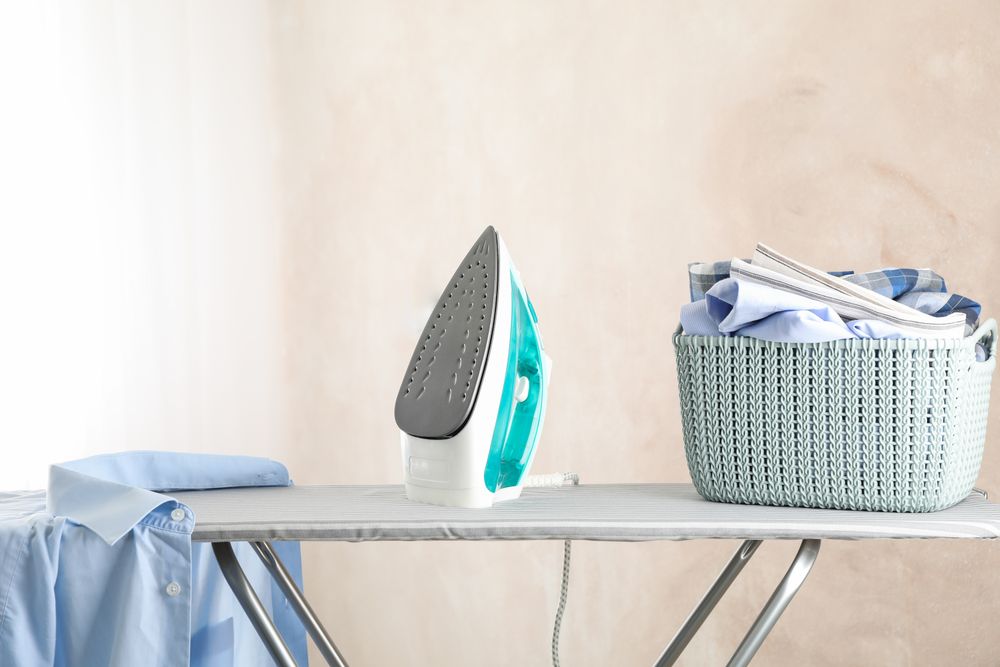 Iron and basket with clear laundry against light background, space for text