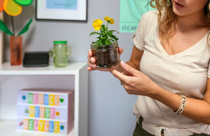 Woman holding a pansy plant inside of glass pot in ecology classroom