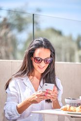 Smiling woman messaging on smartphone while having breakfast in