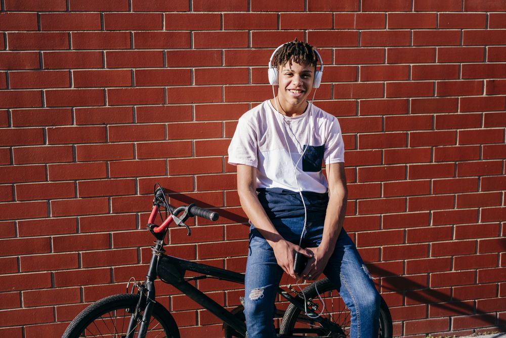 Young happy Black male listening music with smartphone on bike