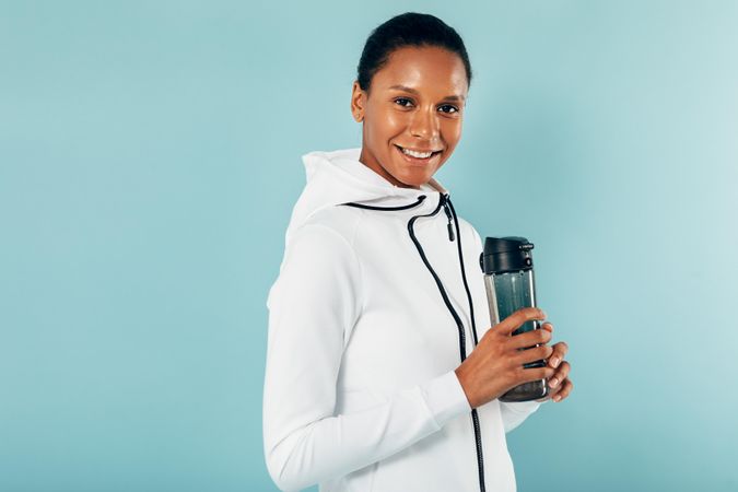 Smiling healthy Black woman with water bottle on blue background