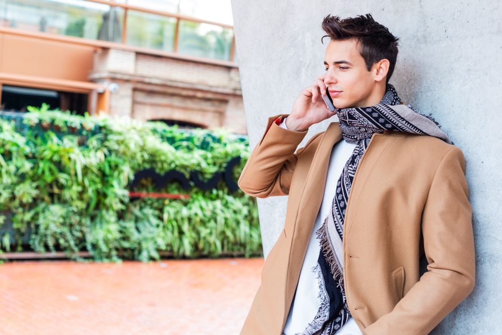 Male in camel coat and scarf standing outside with phone to his ear
