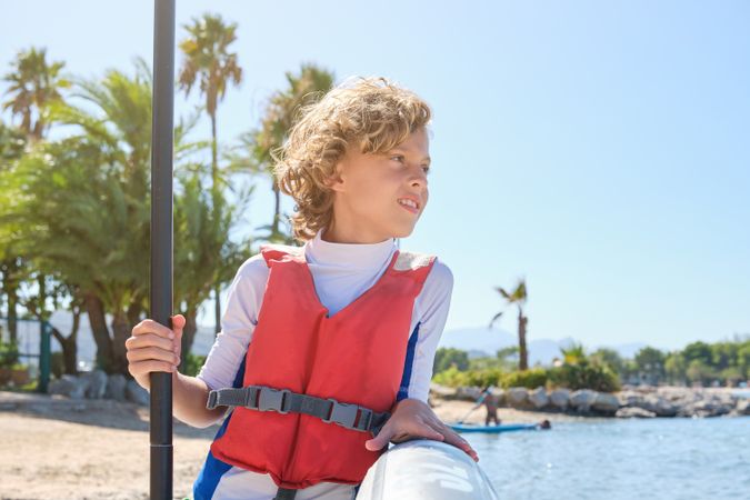 Calm boy leaning on SUP board on beach