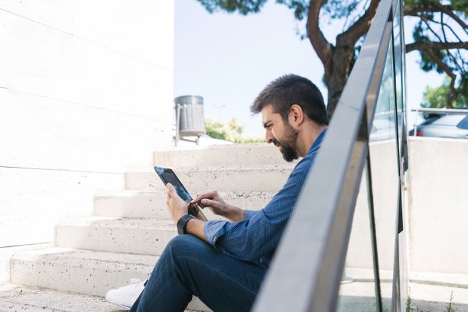 Man sitting on stairs outside checking digital tablet