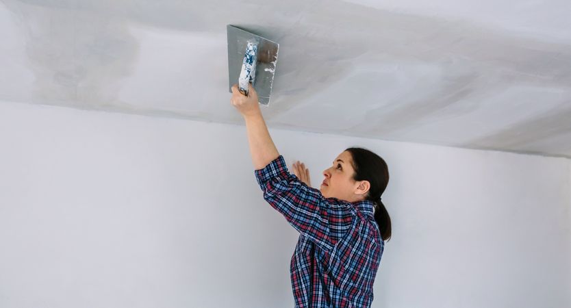 Plasterer smoothing plaster ceiling with the trowel