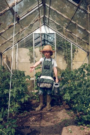 Positive preteen boy gardener with watering can in greenhouse