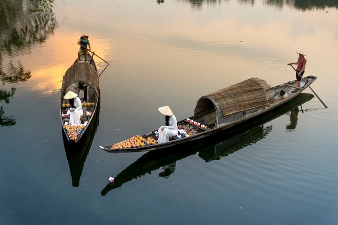 People with conical hats on boats in river at sunset