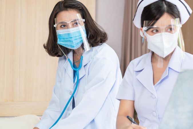 Two female medical professionals in PPE looking around from patient