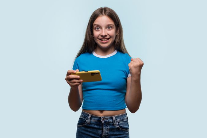 Girl raising fist while looking at smartphone, excited and happy.