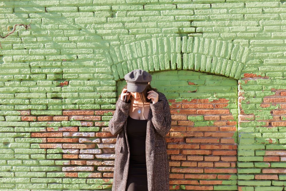 Charming Hispanic woman talking phone near wall
