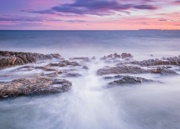 Sea waving near rough rocks during sunset