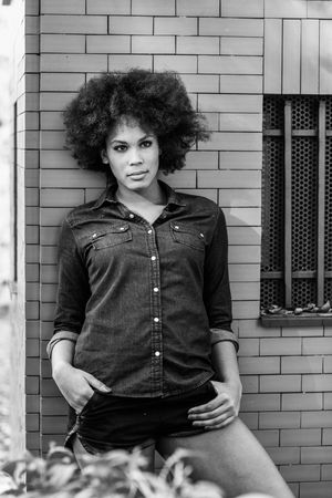 Monochrome shot of female relaxing on building with hands in her pocket