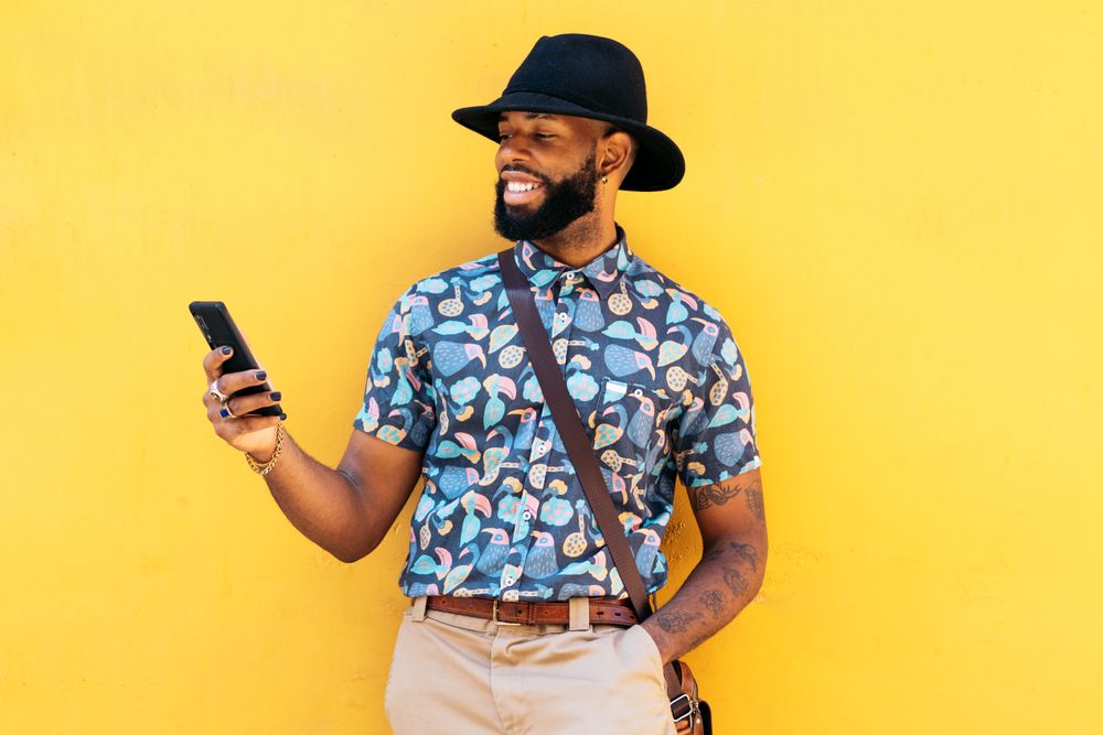 Stylish Black man using smartphone outdoors over yellow background