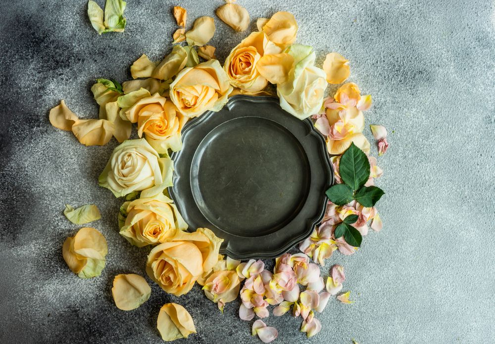 Beautiful floral card concept with fresh rose petals surrounding dark plate on counter